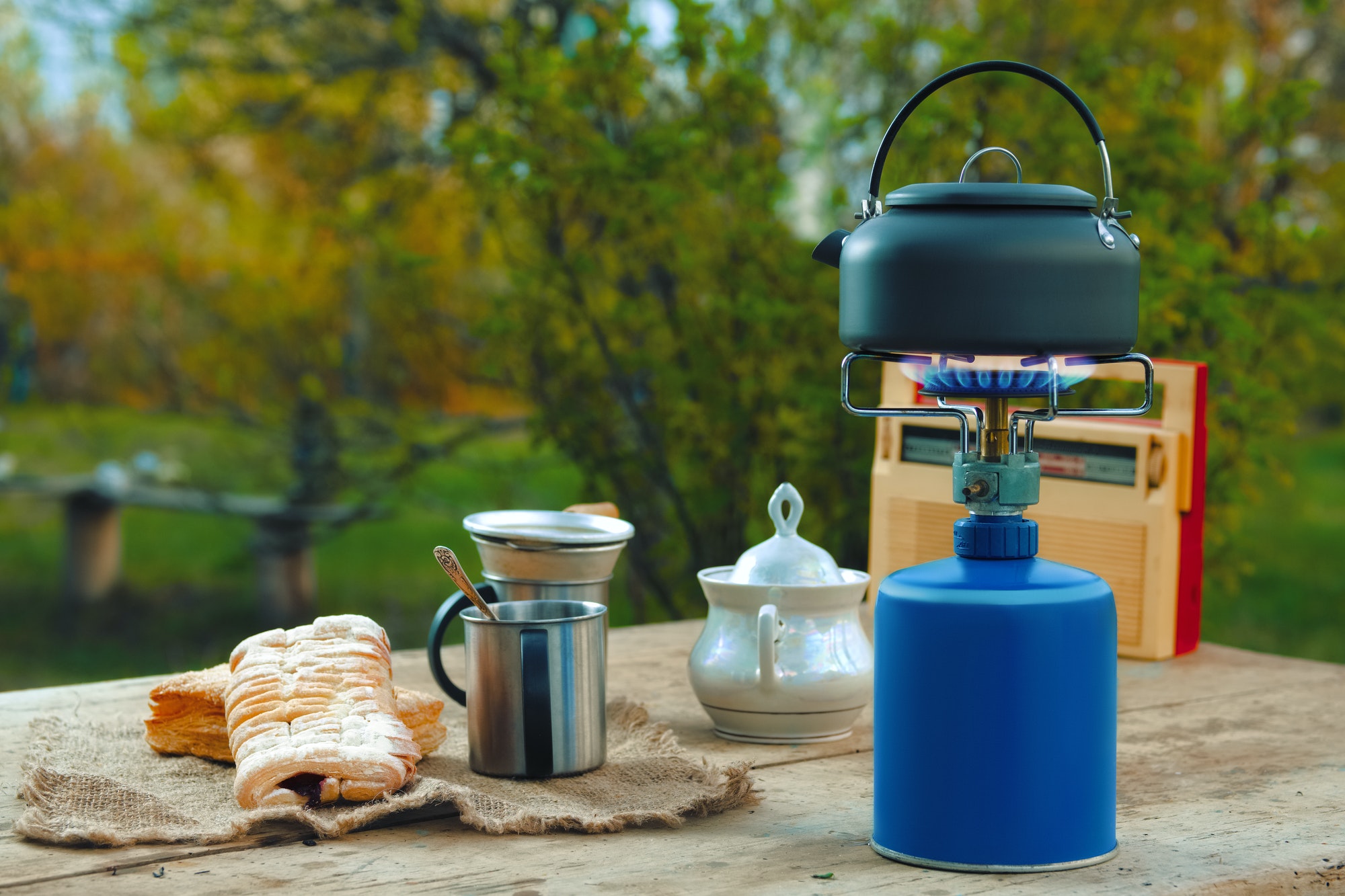 Camping kettle, cups and biscuit on rustic table.
