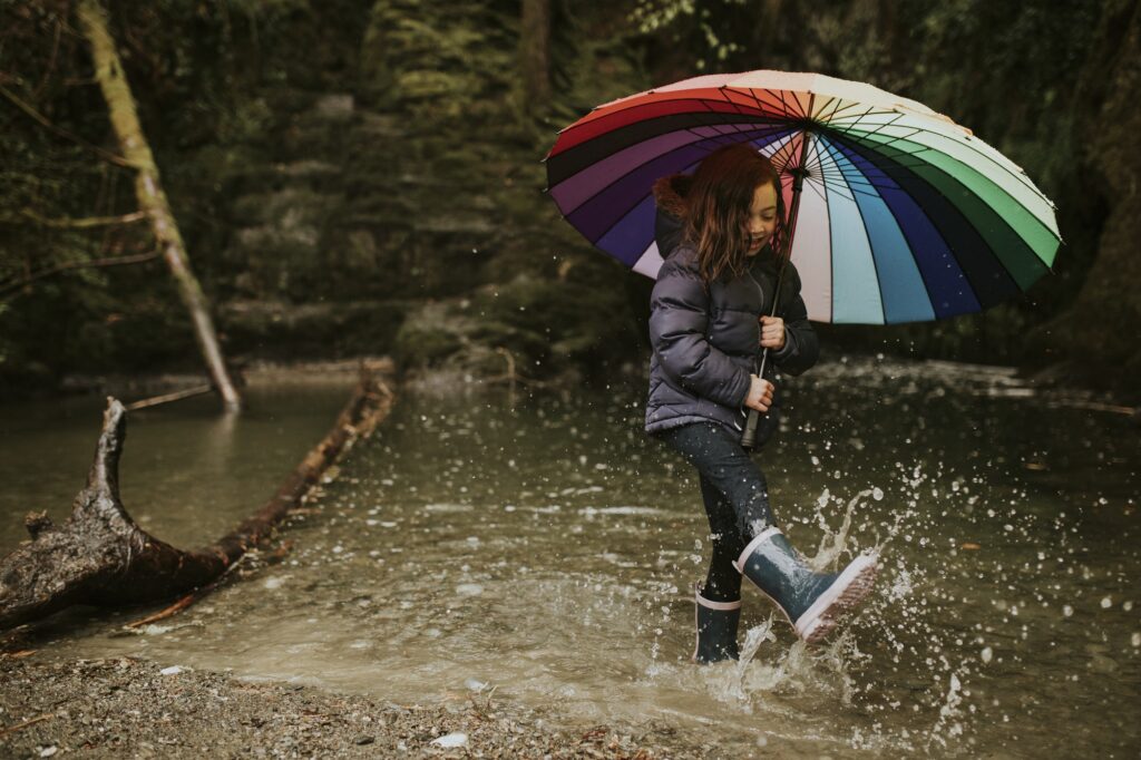 Happy girl playing by the forest lake with an umbrella on a rainy day